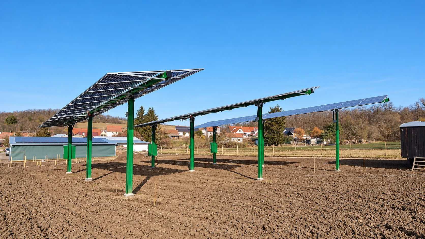 Reálná fotografie ukázkové agrovoltaické konstrukce se solárními panely na zelených sloupech nad polem